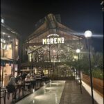 A group of people are sitting outside of a restaurant at night, enjoying their time together.