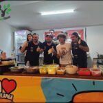 A group of people are standing around a table with food on it, giving a thumbs up.