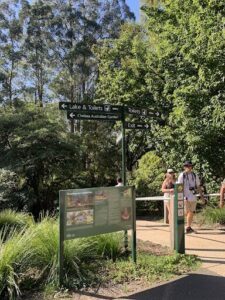 A group of people are standing in front of a sign that points to Lake Toilets and Australian Garden.