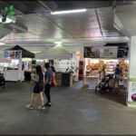 A group of people are walking around a market, with some of them carrying handbags.