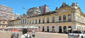 A group of people are walking in front of a large building with a yellow roof.