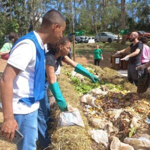 A group of people are working together to sort through a pile of trash, including bags of garbage and a car.