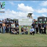 A group of people wearing hard hats pose for a photo in front of a sign that reads "Bem-vindo a fábrica de cavaco."