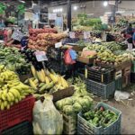 A large assortment of fruits and vegetables are displayed at a market, including bananas, apples, and oranges.