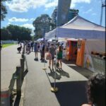 A large crowd of people are gathered around a food stand, with some of them sitting on the ground.