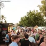A large crowd of people are gathered in a public space, with many of them carrying handbags. The atmosphere appears to be lively and bustling, as the people mingle and interact with one another.