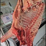 A large cut of meat hangs in a store, ready to be sold.