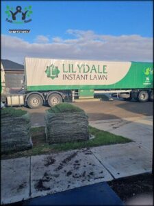 A large green and white truck is parked in front of a house, possibly delivering or picking up lawn care equipment.