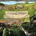 A large green tent with a sign that says "Hmong Veggie" is filled with a variety of fresh vegetables.