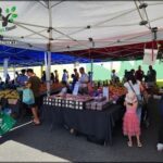 A large group of people are gathered around a fruit stand, with a variety of fruits on display.