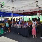 A large group of people are gathered around a fruit stand, with a variety of fruits on display.