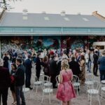 A large group of people are gathered outside of a building, socializing and enjoying each other's company.