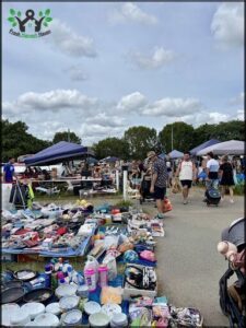 A large group of people are walking around a flea market, with various items for sale.