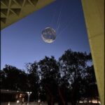 A large, illuminated sphere hangs in the air, suspended by a series of cables.