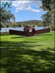 A large metal sculpture is situated in a grassy field near a body of water.