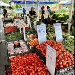 A large outdoor market is filled with fresh produce, including tomatoes and peppers.