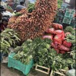 A large pile of carrots and other vegetables are displayed at a market.