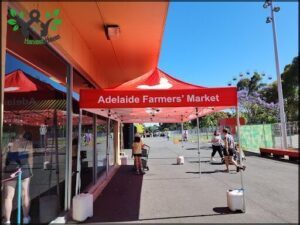 A large red tent is set up in front of a building, advertising the Adelaide Farmers' Market.