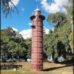 A large red tower stands in a park, surrounded by trees.