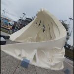 A large white sculpture of a wave is on display in a park.