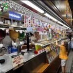 A little girl is standing in front of a candy display, reaching for a piece of candy.