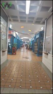 A long hallway with a variety of shops and a large light hanging from the ceiling.