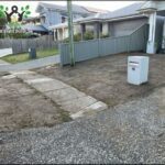 A mailbox is sitting on a dirt patch in front of a house.