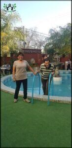 A man and woman are standing in a swimming pool, holding onto blue handles.