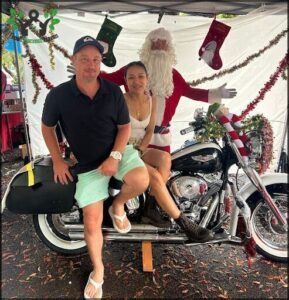 A man and woman sit on a motorcycle with Santa Claus on the back.