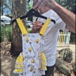 A man holds up a yellow and white dress with yellow bees on it.