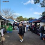 A man in a black jacket walks past a food stand at a market.
