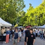 A man in a black shirt walks past a group of people at a market.