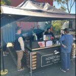 A man in a blue shirt is standing in front of a coffee shop, talking to a woman who is behind the counter.