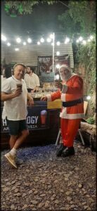 A man in a Santa suit holds a beer while standing next to another man.
