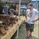 A man in a white shirt is looking at a table full of wooden items.