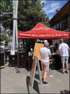A man is standing in front of a red tent, which is advertising a natural spice essential by Ragini.