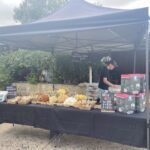 A man is standing in front of a table filled with food, possibly selling or preparing it.