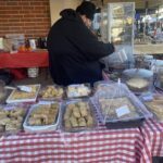 A man is standing in front of a table filled with various pastries and desserts.