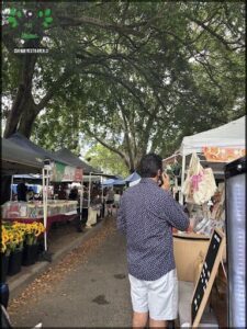 A man is talking on his cell phone while walking down a street with a market stand in the background.