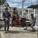 A man plays the drums while two other men play the guitar and the cello.
