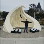 A man poses in front of a large white sculpture.
