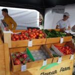 A man stands behind a table filled with fresh vegetables, including tomatoes and peppers.