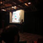 A man stands in front of a screen, possibly giving a presentation or lecture.