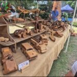 A man stands in front of a table filled with wooden toy cars and trucks.