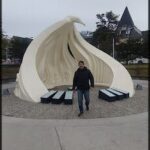 A man stands in front of a white sculpture of a bird.