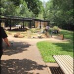 A man walks his dog in a park with a bench nearby.