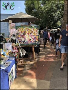 A man walks past a painting of a doll with a pink bow, while a woman with a pink shirt stands nearby.