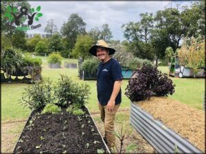 A man wearing a hat and blue shirt is standing in a garden.