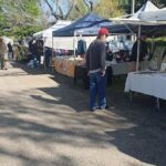 A man wearing a red hat is standing in front of a table at a market.