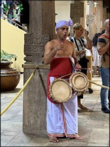 A man wearing a white outfit and a red sash is holding a drum.